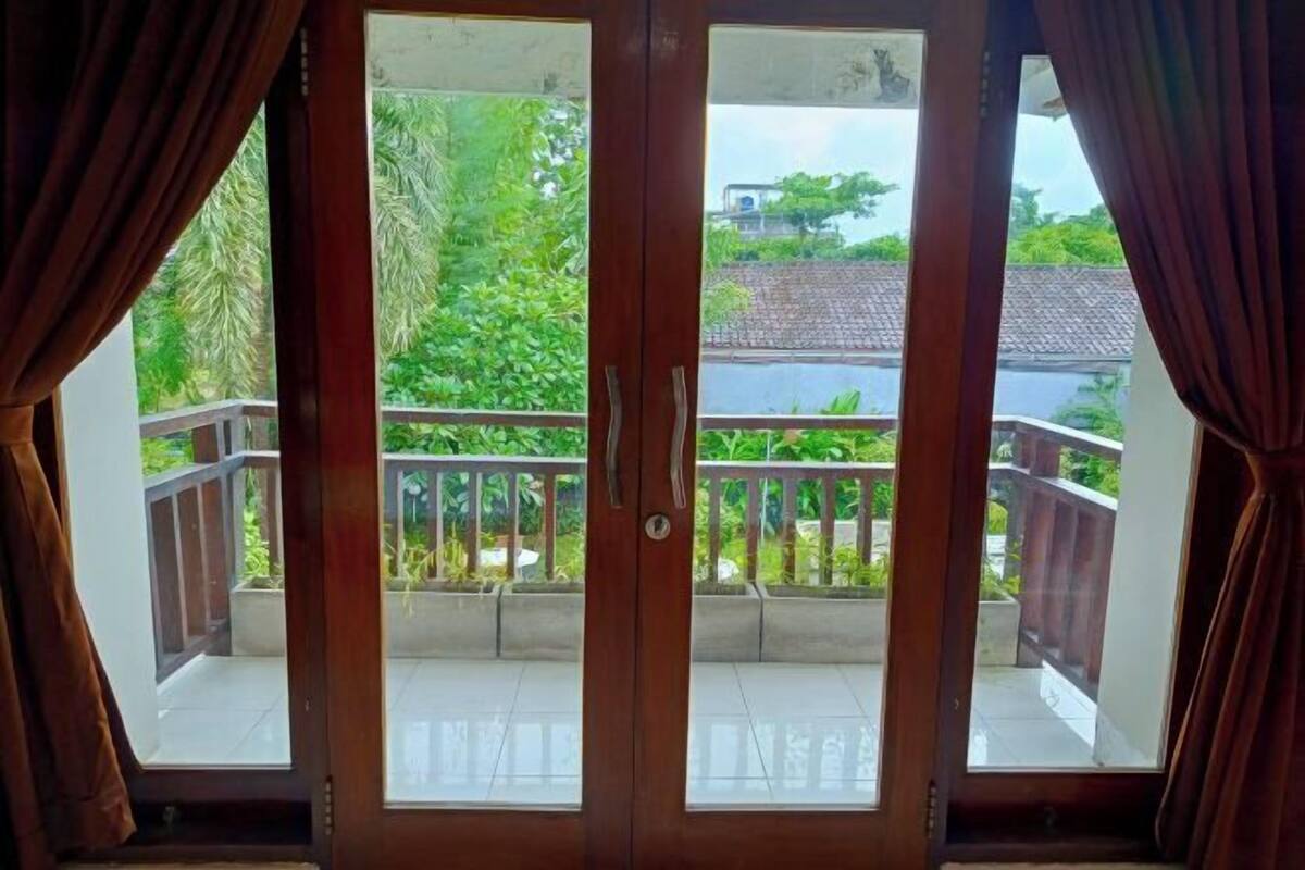 A wooden door with a view of a balcony with a railing and greenery outside.