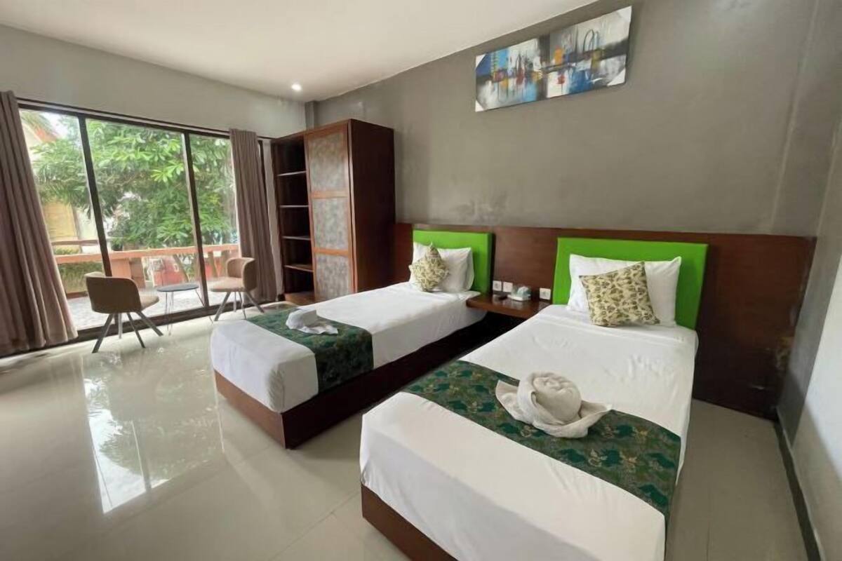 A hotel room with two beds, a large window, a wardrobe, and a painting on the wall.
