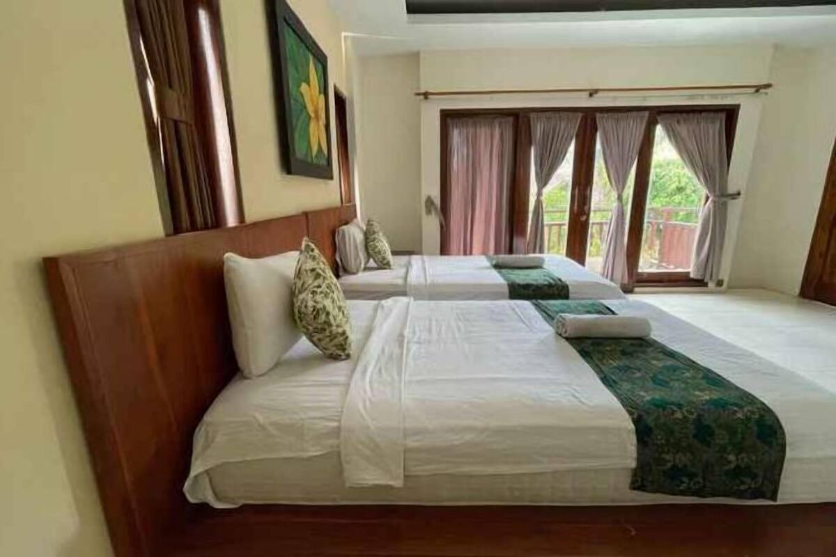 A hotel room with two beds, a wooden headboard, a large window with curtains, and a painting on the wall.