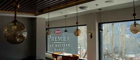 Un interior moderno con lámparas colgantes, un ventanal con vistas a las montañas, y un letrero que dice "Premier West Western Hunza".