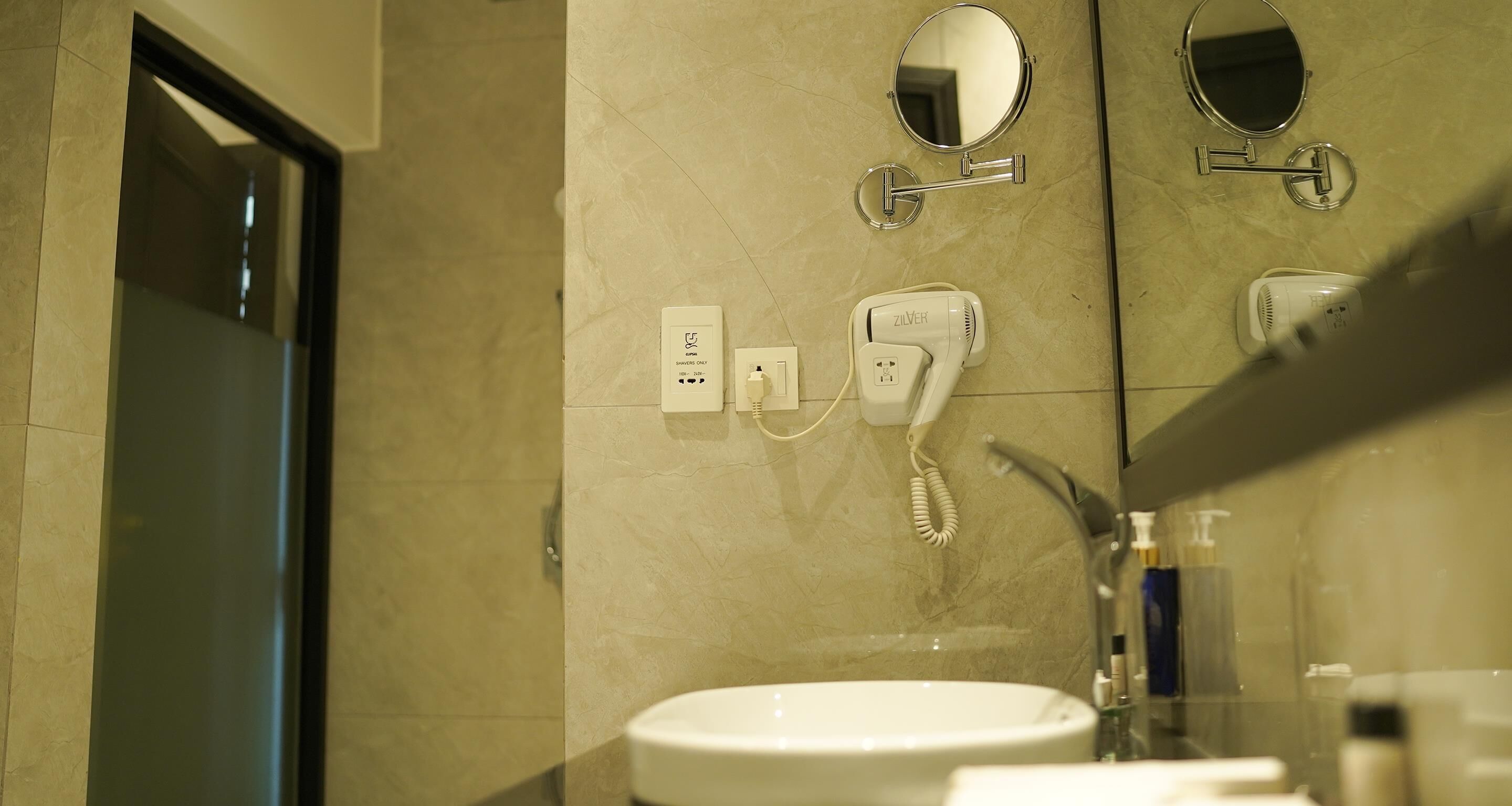 A bathroom with a sink, two mirrors, a hairdryer, and a towel rack.
