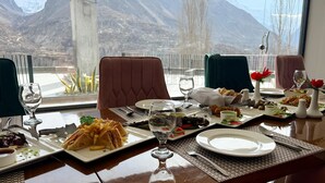 A dining table set with various dishes, glasses, and cutlery, with a mountain view in the background.