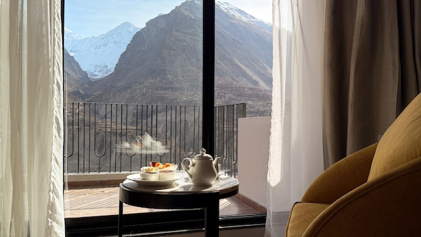 A balcony with a table set for tea, a chair, and a mountain view.