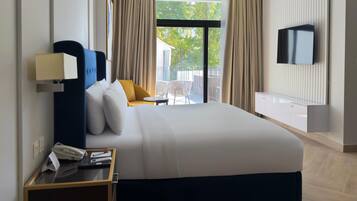 Quarto de hotel com cama grande, mesa de cabeceira com luminária, TV fixada na parede e vista para o exterior através de uma porta deslizante.