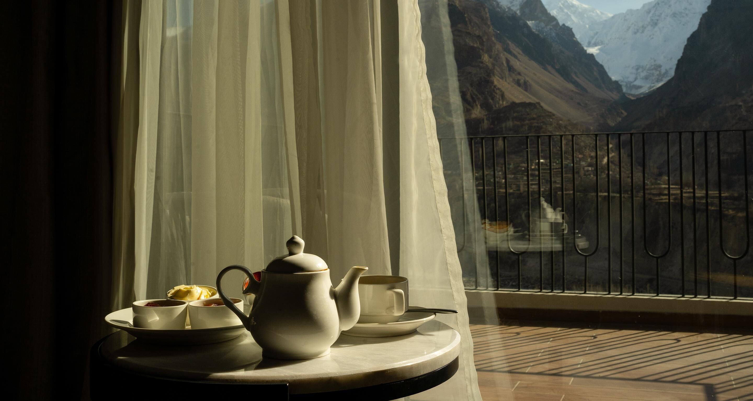 Una mesa con tetera, tazas y un plato de comida junto a una ventana con vista a la montaña.