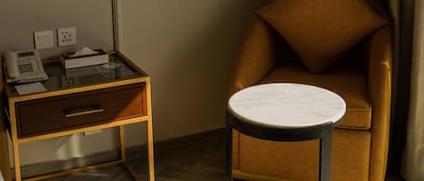 Una habitación de hotel con una mesita de noche de madera, un teléfono, una caja de pañuelos y una pequeña mesa redonda con tapa de mármol.