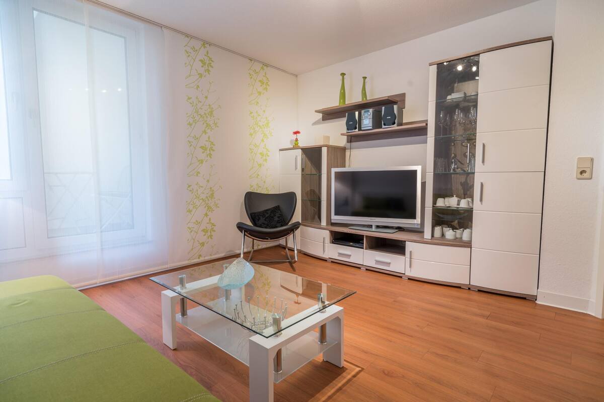 Un salon moderne avec une table basse en verre, un téléviseur à écran plat, un canapé et un meuble avec des portes en verre.