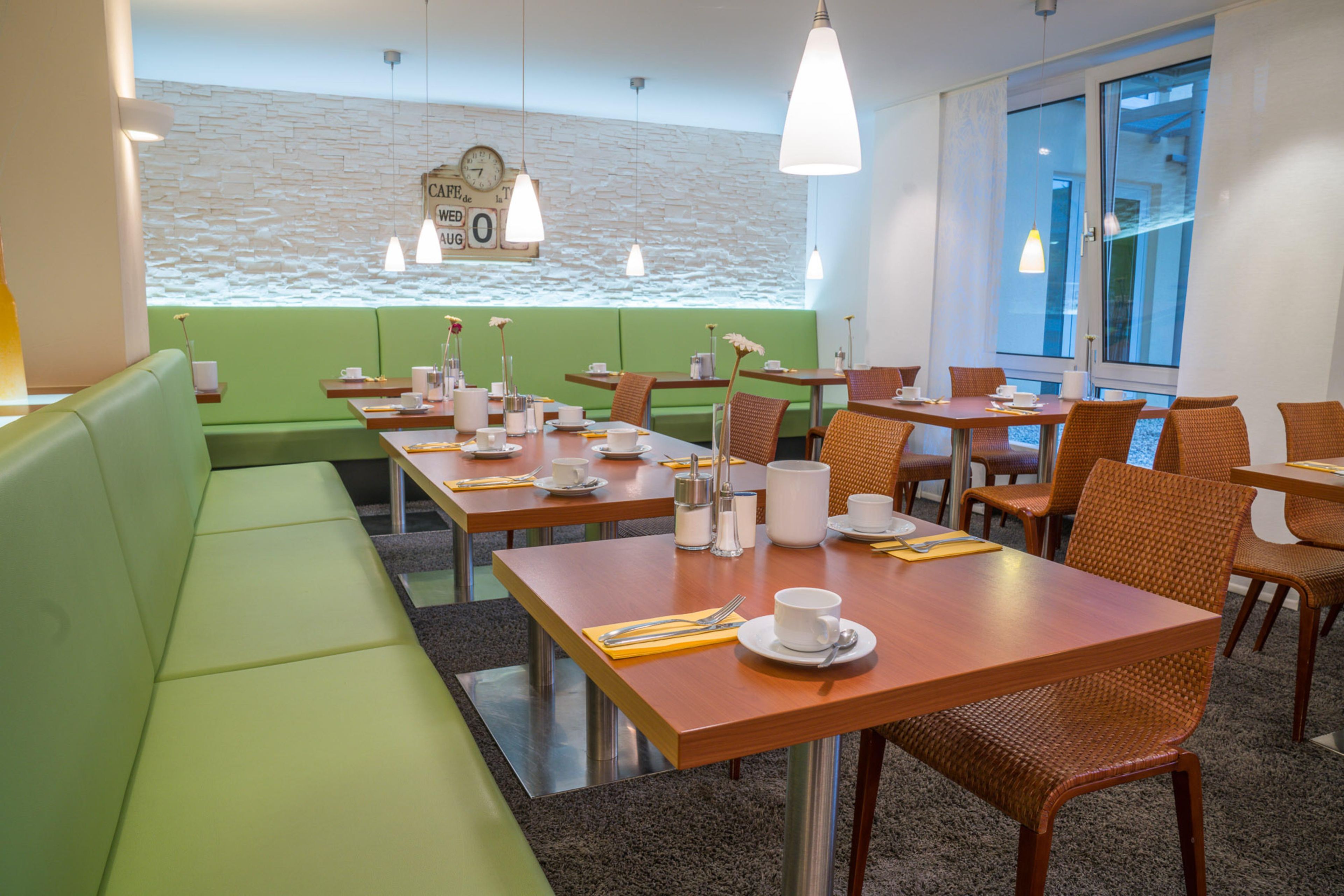 Um restaurante com assentos em verde, mesas de madeira e cadeiras de vime.