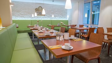 Um restaurante com assentos em verde, mesas de madeira e cadeiras de vime.