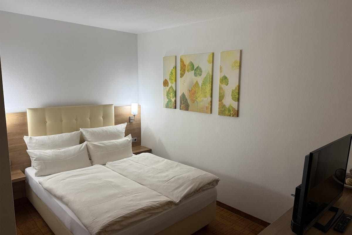 Un lit bien fait, avec du linge de lit blanc, une tête de lit et une table de chevet sur laquelle se trouve une lampe.
