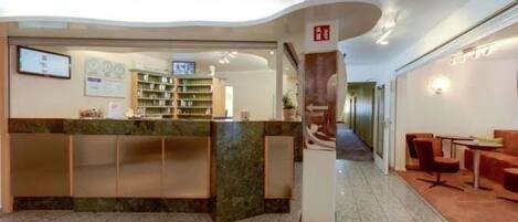 Vestíbulo de hotel con mostrador de recepción, zona de estar y escalera que lleva a otro piso.