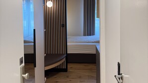 A narrow hallway leading to a bedroom with a bed, a window with curtains, and a striped wall. - Residenzhotel Stuttgart Airport, Sure Hotel Collection by BW (Steinenbronn)