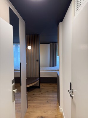 A narrow hallway leading to a bedroom with a bed, a window with curtains, and a striped wall. - Residenzhotel Stuttgart Airport, Sure Hotel Collection by BW (Steinenbronn)