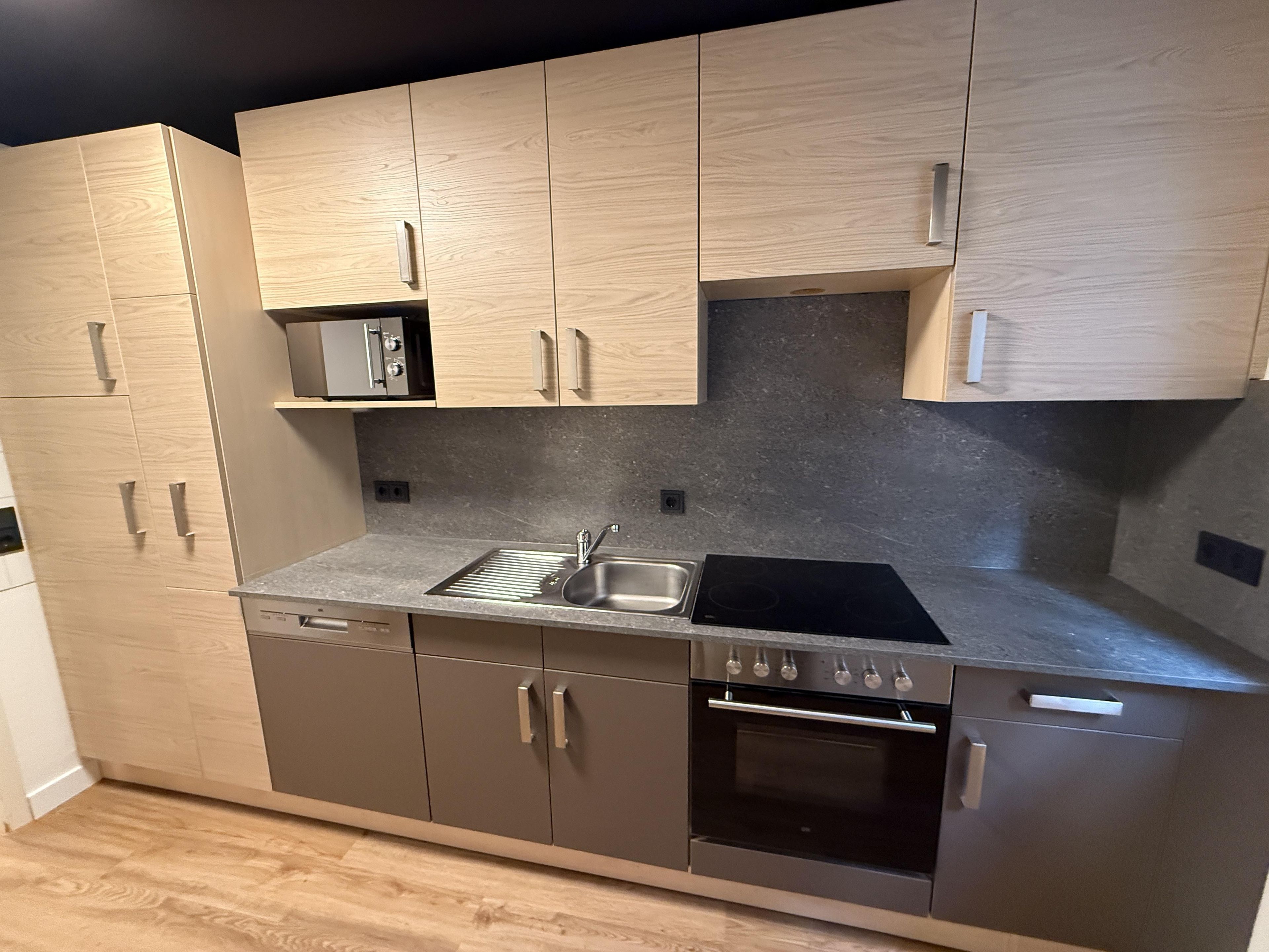 A modern kitchen with wooden cabinets, a built-in oven, and a stainless steel sink.