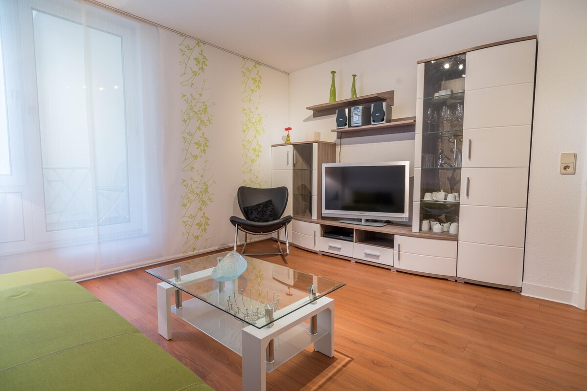 A modern living room with a glass coffee table, a flat-screen TV, a sofa, and a cabinet with glass doors.