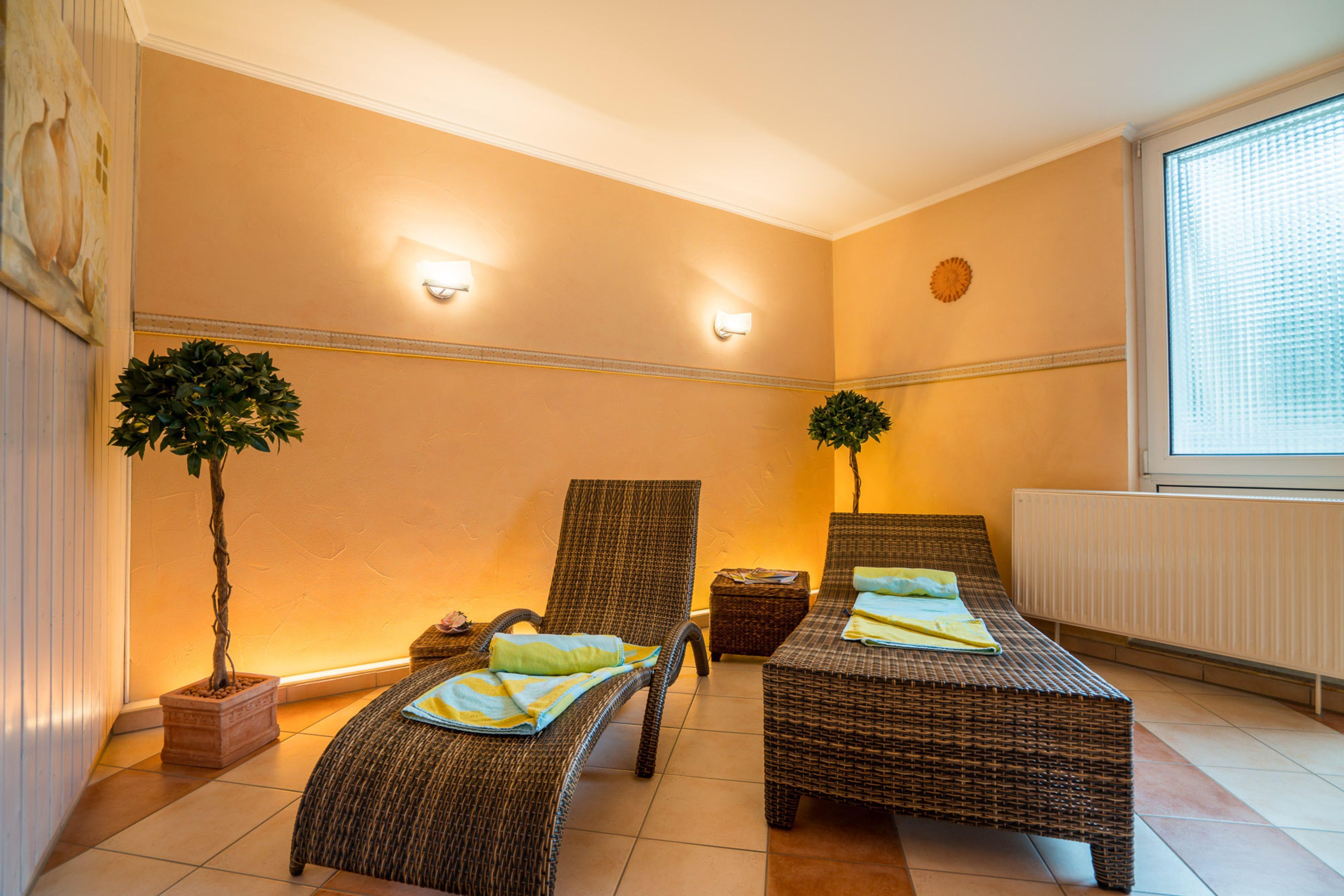 Ein Zimmer mit zwei Korbmöbelbetten, einem kleinen Tisch, zwei Topfpflanzen und einem Fenster mit Jalousien.