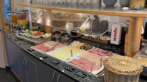Buffet com diversas opções de comida, incluindo carnes, queijos e saladas, com uma placa de Nutella à vista.
