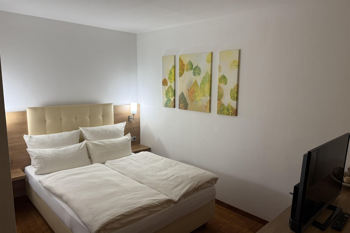 A neatly made bed with white linens, a headboard, and a bedside table with a lamp.