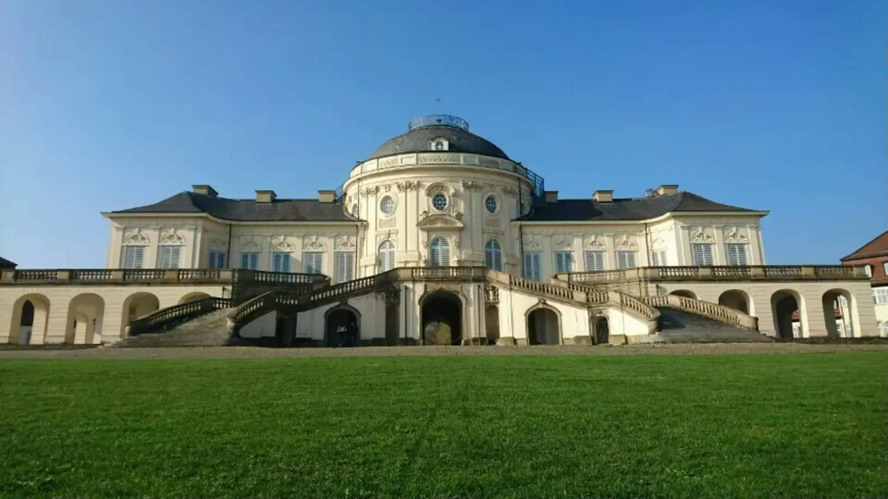 A large, classical building with a central dome, symmetrical wings, and a grand staircase leading to the entrance.