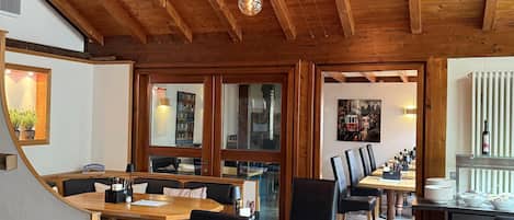 Un restaurante con vigas de madera, lámparas colgantes y una combinación de mesas y sillas de madera y tapicería.