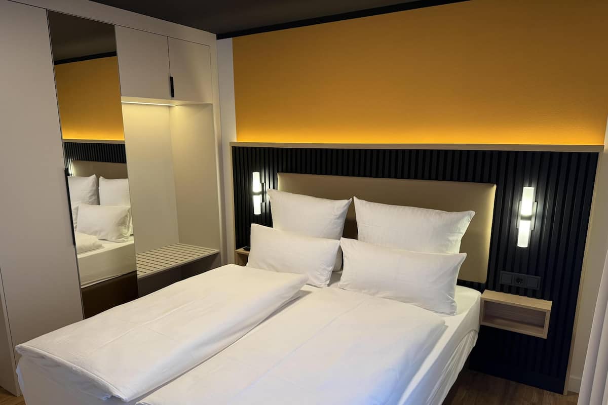 Une chambre d’hôtel avec un grand lit, une table de chevet, une commode, un miroir et un luminaire fixé au mur.
