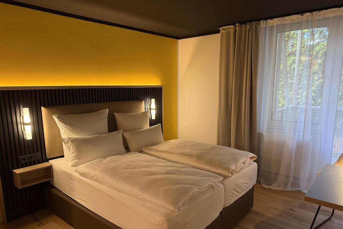 Un lit bien fait, avec une tête de lit, une table de chevet et une fenêtre avec des rideaux.