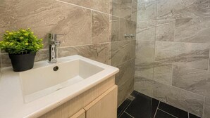 Une salle de bain avec un lavabo blanc, une plante en pot et des carreaux de marbre beige.