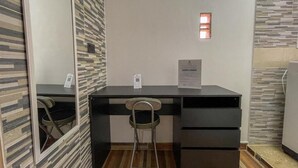 Une pièce de taille modeste, équipée d’un bureau, d’une chaise et d’un petit réfrigérateur.