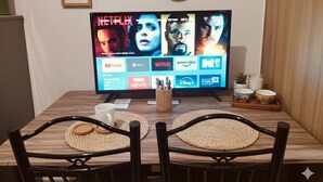 A television displaying various streaming services, a wooden table with woven placemats, and a decorative wall with framed artwork. - Mall of Asia - Cheap Accommodations (Pasay)