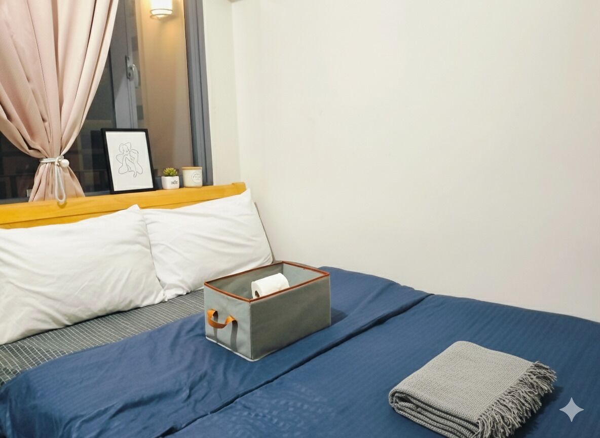 A neatly made bed with a blue bedspread, a grey throw blanket, and a grey storage box with a handle.