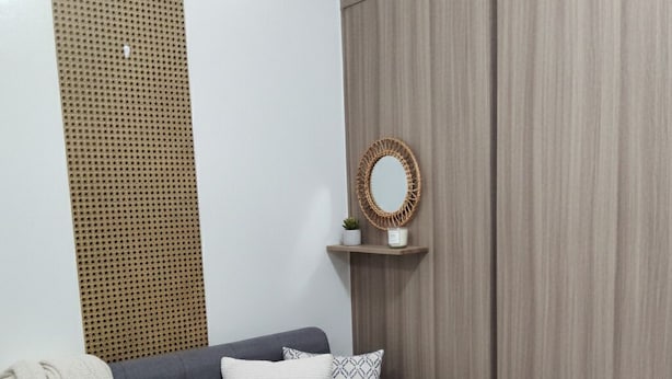 A grey sofa with a white throw blanket and patterned pillows, a woven basket, and a wall-mounted shelf with a mirror and small plant. - Mall of Asia - Cheap Accommodations (Pasay)