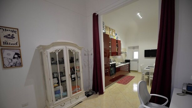 A room with a white cabinet, a dining area with a red rug, and a television on the wall. - dimorarte (Minervino Murge)