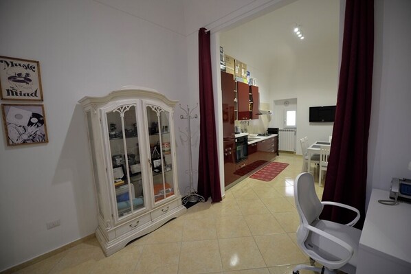 Una habitación con un armario blanco, una zona de comedor con un tapete rojo y un televisor en la pared.