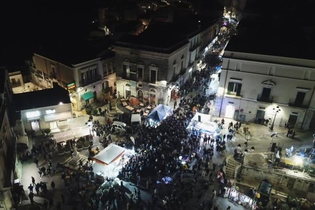 Vista aérea de una plaza urbana concurrida de noche, con edificios y farolas.