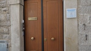 A wooden double door with a brass plate and a keyhole, a wall-mounted sign, and a stone wall. - dimorarte (Minervino Murge)