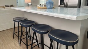 Eine moderne Küche mit Marmorarbeitsplatte, einer blauen Vase und drei Barhocker.