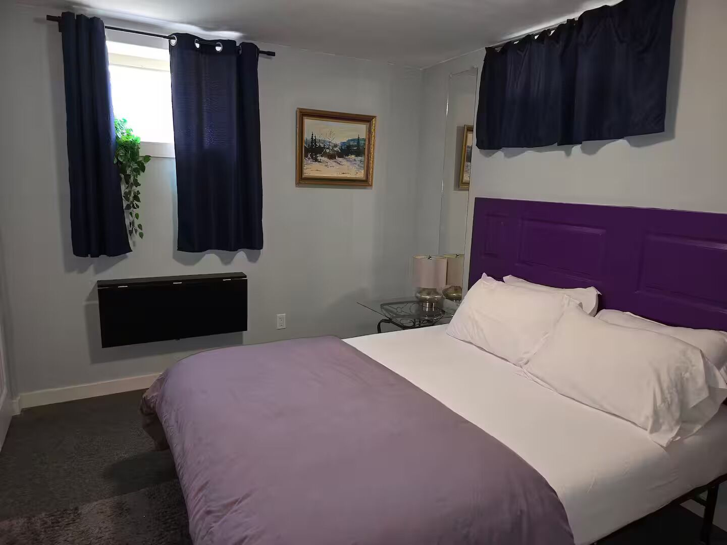 Ein Schlafzimmer mit einem Bett, einem Nachttisch, einem Wandheizkörper und einem Fenster mit Vorhängen.