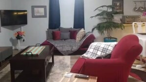 Een woonkamer met een bank, een rode fauteuil, een televisie en een potplant.