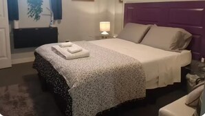 Hotelkamer met een bed, nachtkastje, lamp, raam met gordijnen en een aan de muur hangend schilderij.