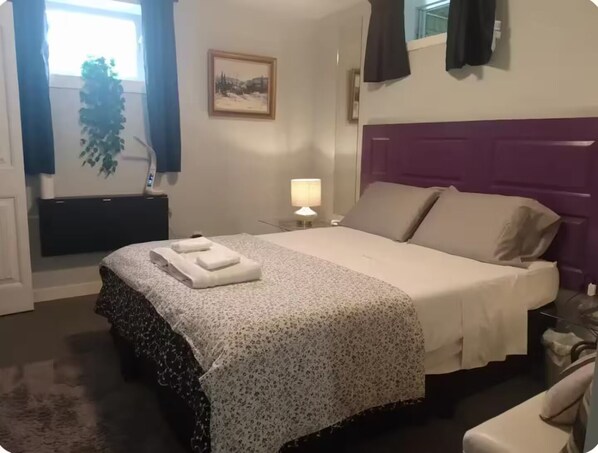 Una habitación de hotel con una cama, una mesita de noche, una lámpara, una ventana con cortinas y un cuadro colgado en la pared.