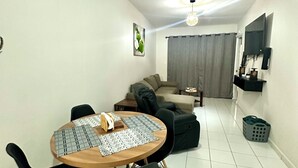 A modern living room with a dining area, a ceiling fan, a flat-screen TV, and a grey curtain.