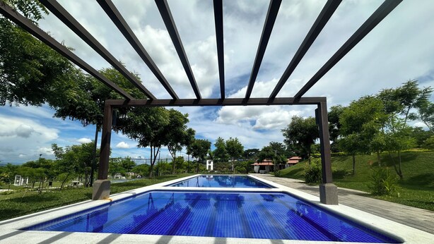 A rectangular swimming pool with blue tiles, surrounded by a paved walkway and a pergola structure.