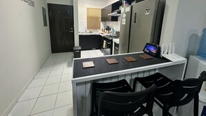 A modern kitchen with a black and white tiled floor, a central island with chairs, a refrigerator, and a wall-mounted clock.
