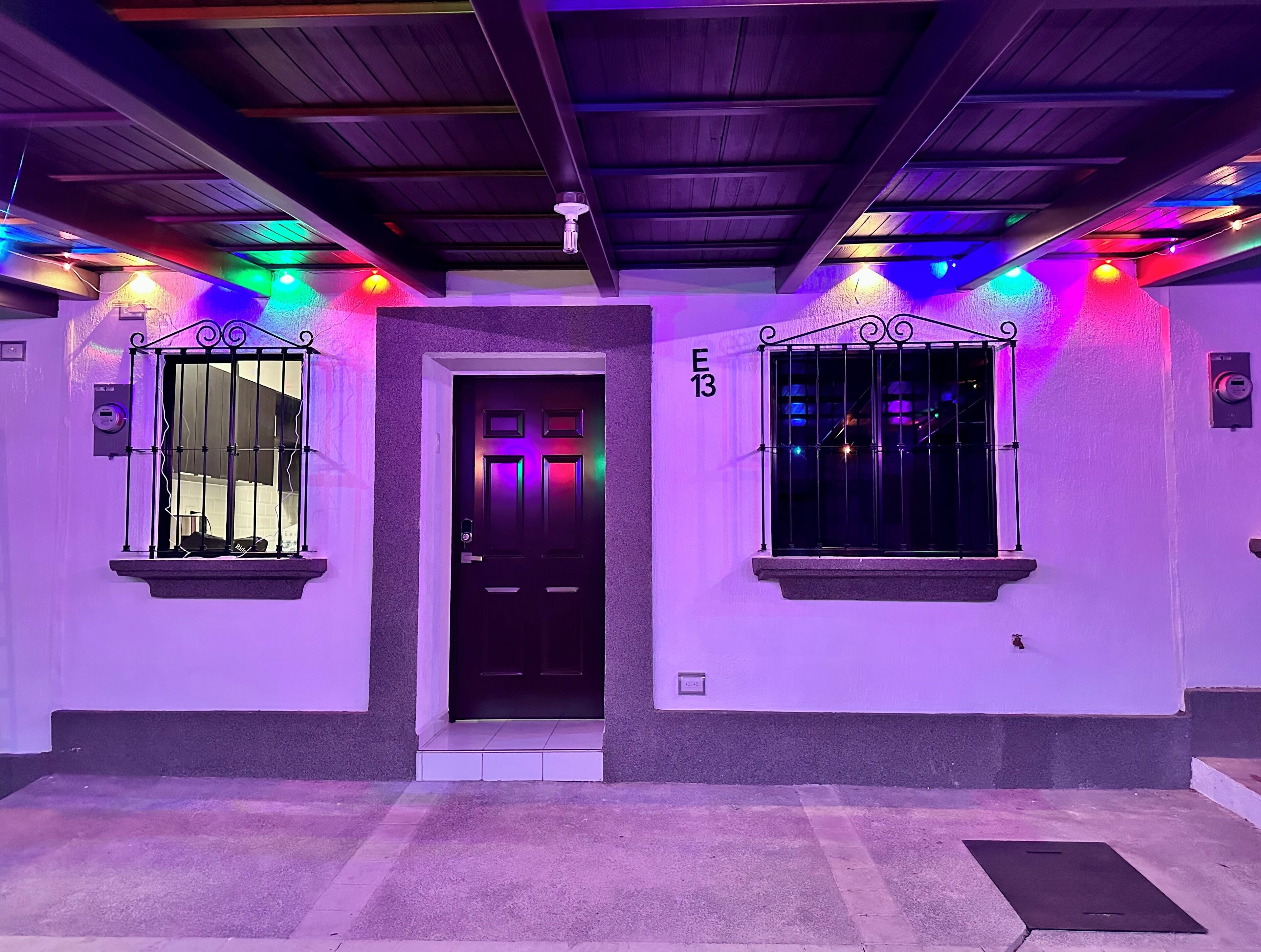 Un passadís amb una porta, dues finestres amb reixes metàl·liques i il·luminació colorida.