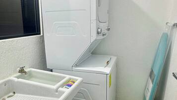 A compact laundry room with a washing machine, a dryer, and a small sink with a soap dispenser.