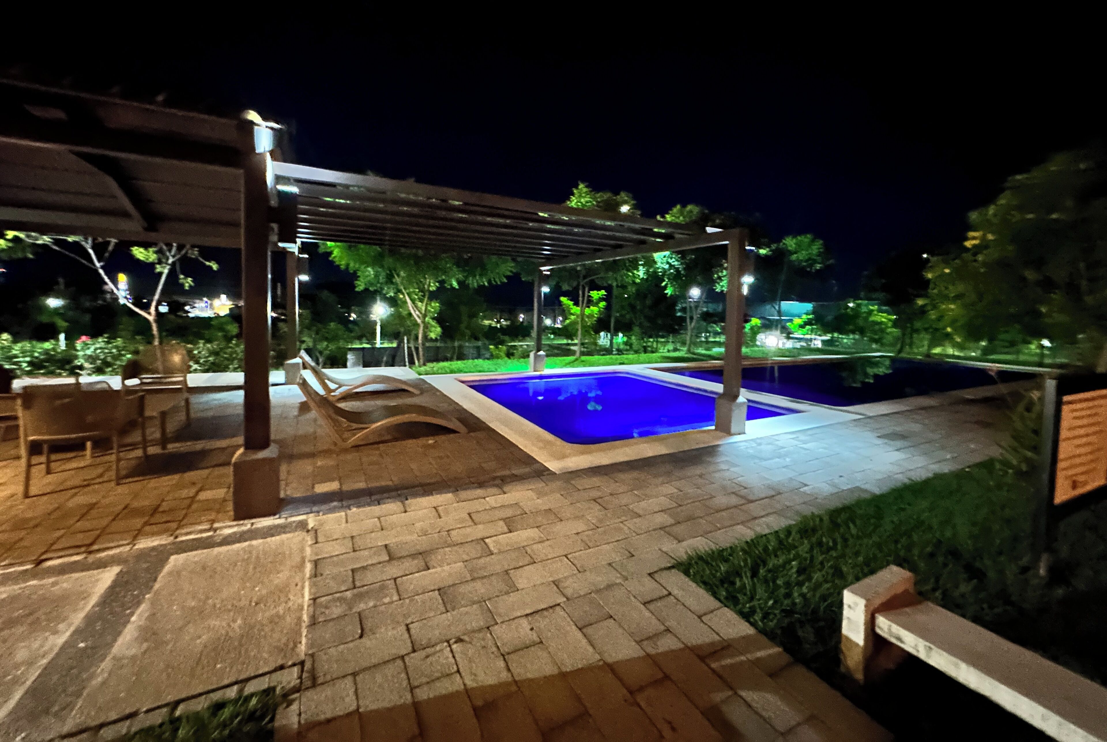 A nighttime outdoor pool area with a covered seating area and a brick pathway.
