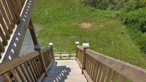 A wooden staircase leading to a building with a grassy area and yellow flowers in the background.