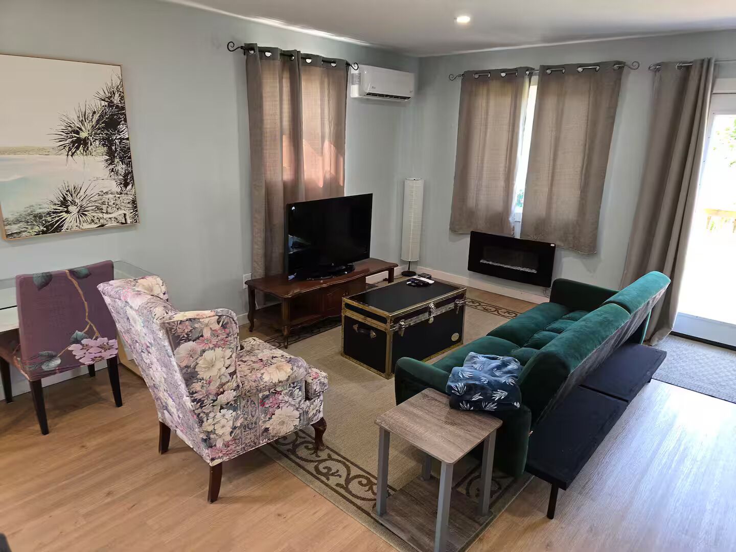 A living room with a green sofa, a floral armchair, a TV, a fireplace, and a painting on the wall.