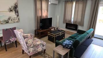 A living room with a green sofa, a floral armchair, a TV, a fireplace, and a painting on the wall.