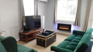A living room with a TV, a fireplace, and green furniture.